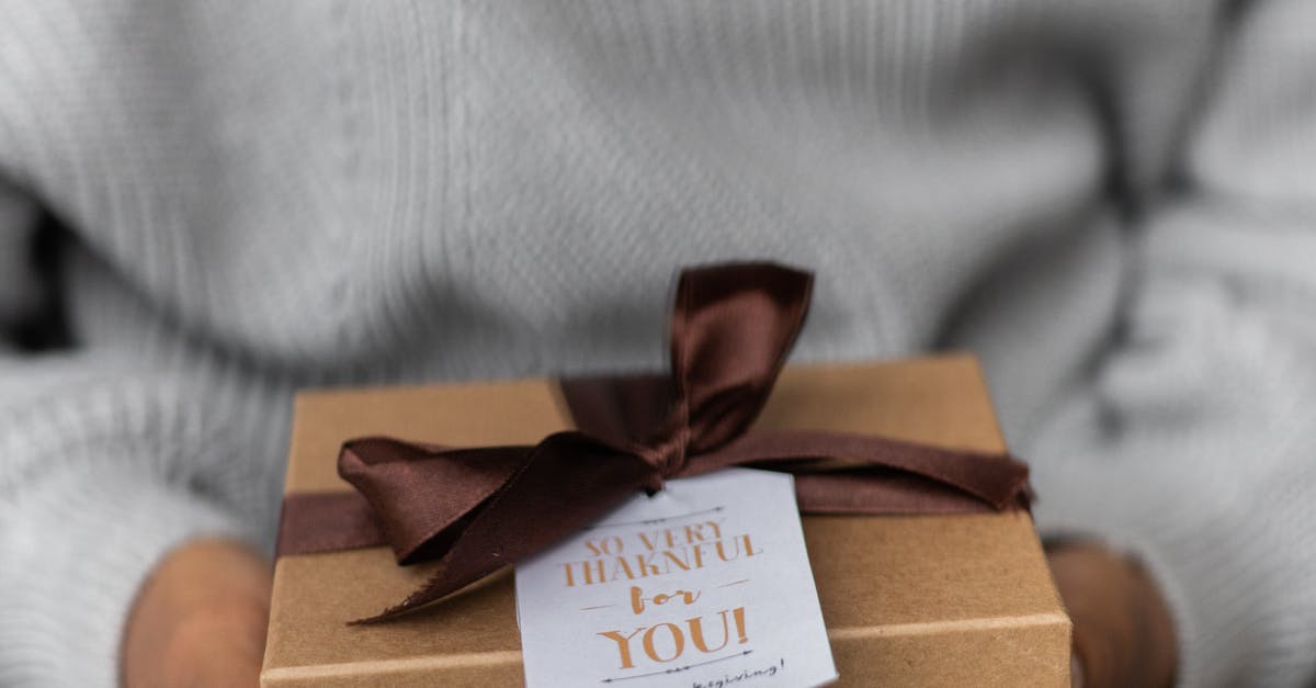 Crop unrecognizable female in knitted sweater with carton present box with bow and small postcard